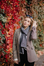 Frau kombiniert Strickschal in Grau-Melange mit kariertem Mantel im Herbst-Outfit.