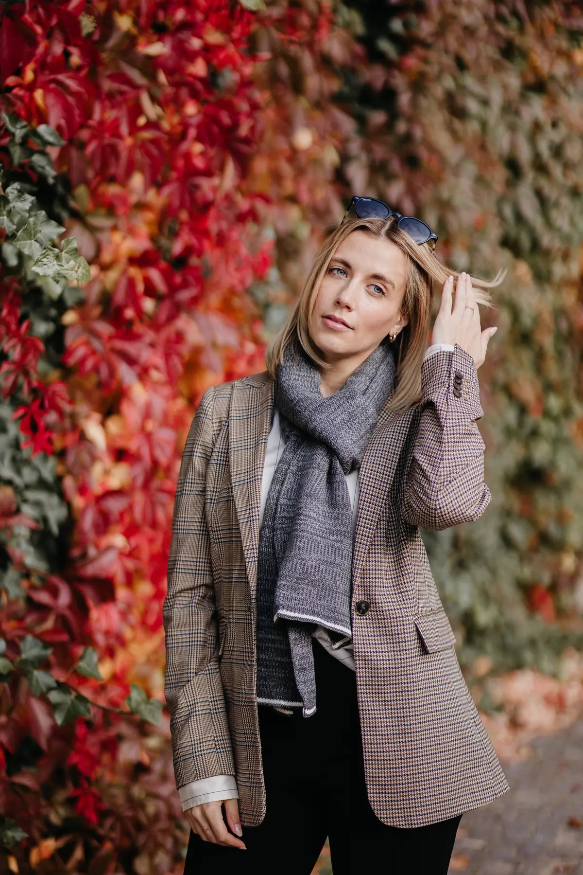 Frau kombiniert Strickschal in Grau-Melange mit kariertem Mantel im Herbst-Outfit.