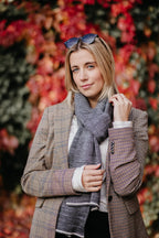 Frau trägt Strickschal in Grau-Melange zu kariertem Mantel im Außenbereich.