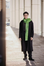 Mann trägt Strickschal in Grün-Melange zu dunklem Mantel im urbanen Umfeld.