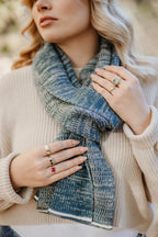 Strickschal in Petrol-Melange mit feiner Strickstruktur, um den Hals getragen.