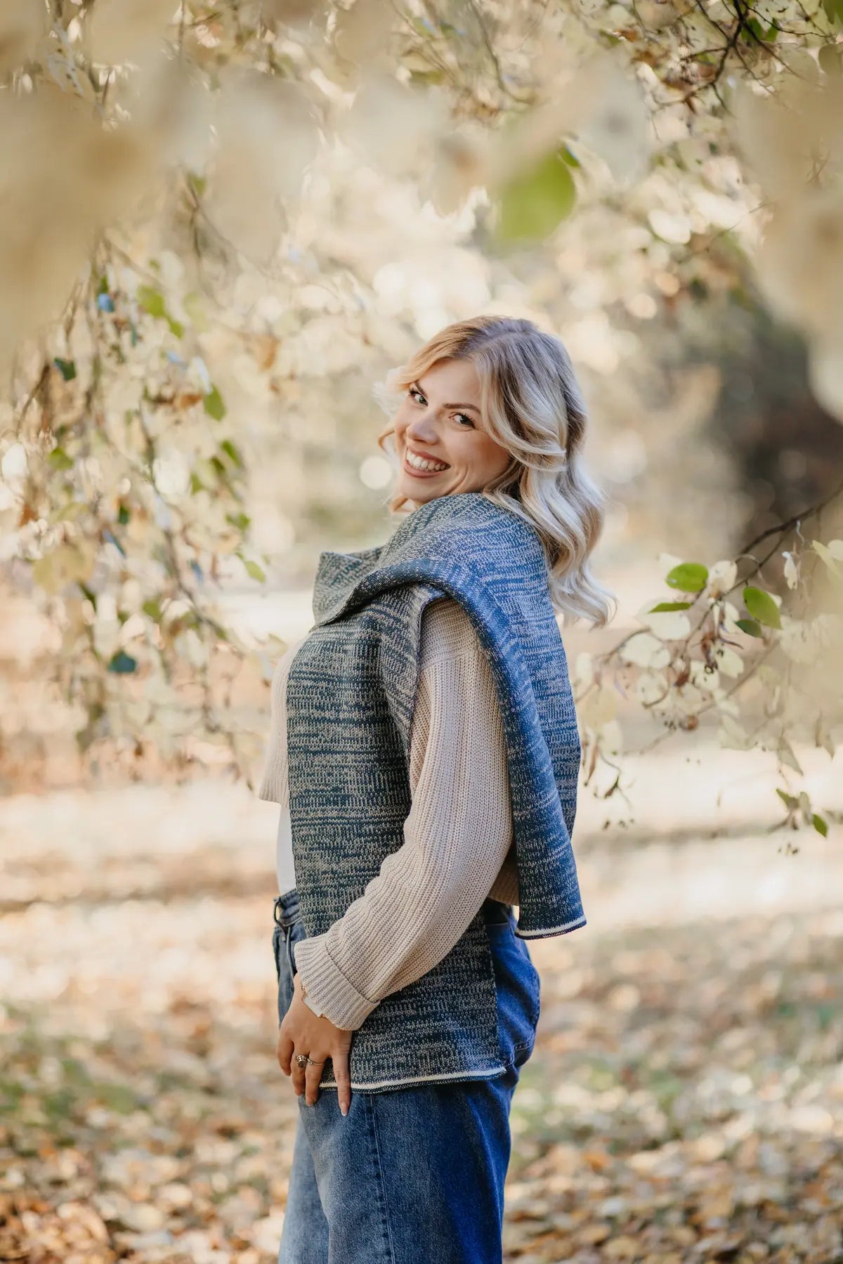 Frau trägt Strickschal in Petrol-Melange locker über die Schultern im Outdoor-Motiv.